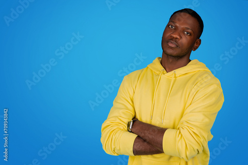 A confident African man stands with arms crossed wearing a yellow hoodie
