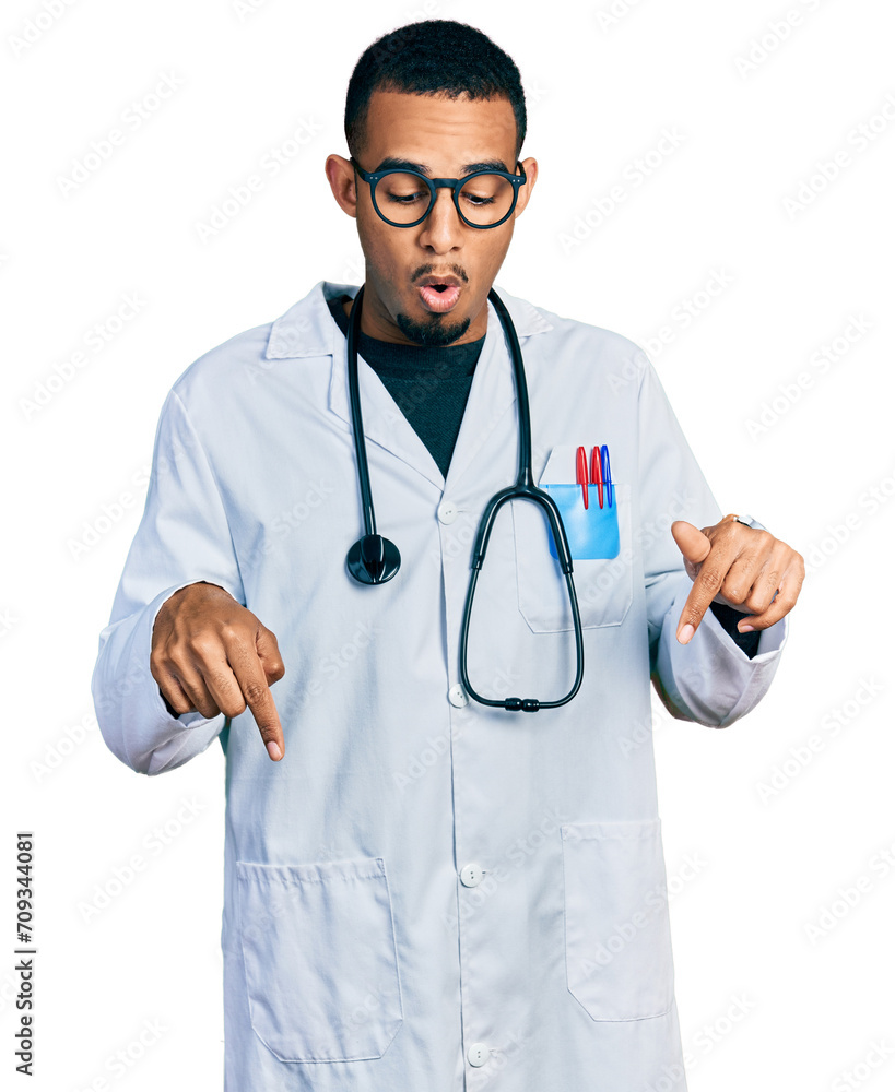 Young african american man wearing doctor uniform and stethoscope pointing down with fingers showing advertisement, surprised face and open mouth