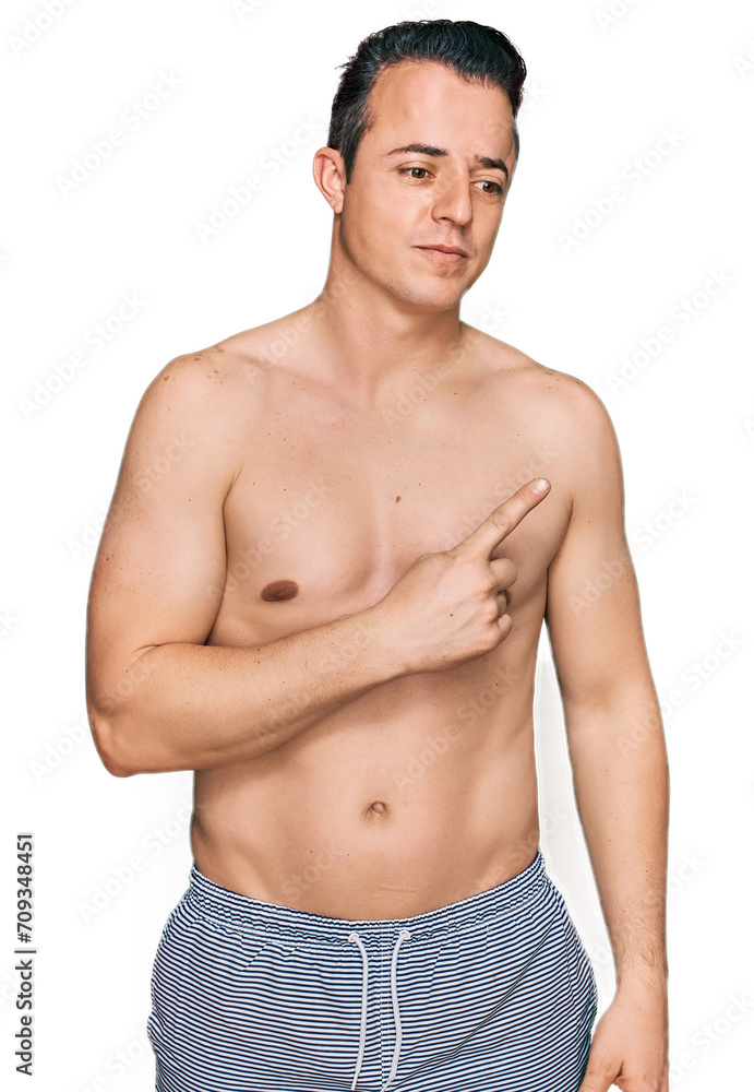 Fototapeta premium Handsome young man wearing swimwear shirtless pointing with hand finger to the side showing advertisement, serious and calm face