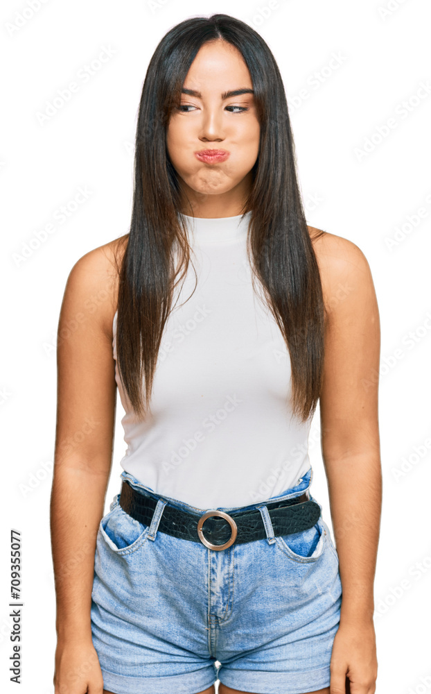 Young beautiful hispanic girl wearing casual clothes puffing cheeks with funny face. mouth inflated with air, crazy expression. Young beautiful hispanic girl wearing casual clothes puffing cheeks with funny face. mouth inflated with air, crazy expression.