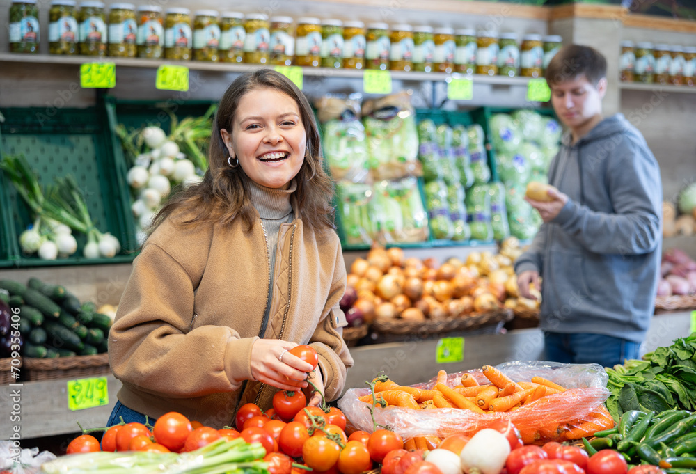 Young female shopper selects and buys tomatoes in a supermarket