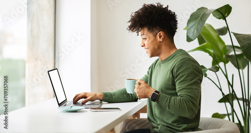 Positive cool african american guy using laptop at cafe photo