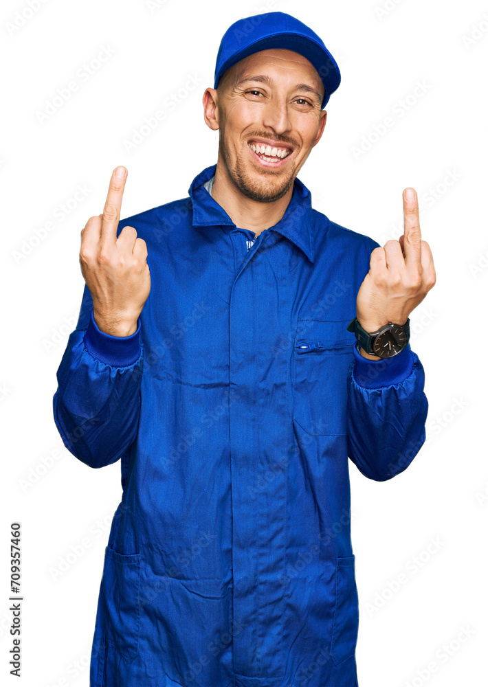 Bald man with beard wearing builder jumpsuit uniform showing middle finger doing fuck you bad expression, provocation and rude attitude. screaming excited