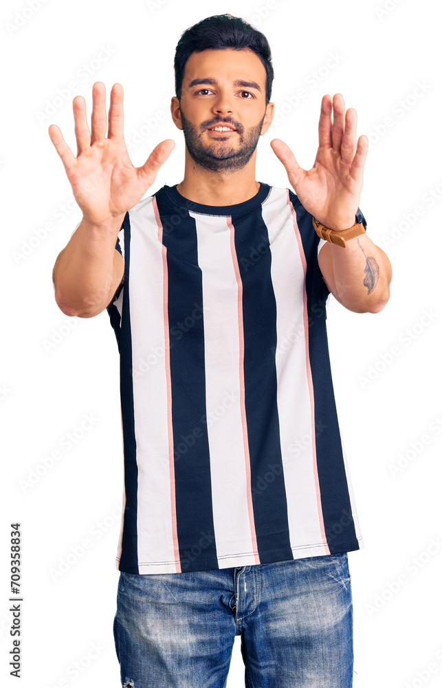 Fototapeta premium Young handsome hispanic man wearing striped tshirt afraid and terrified with fear expression stop gesture with hands, shouting in shock. panic concept.