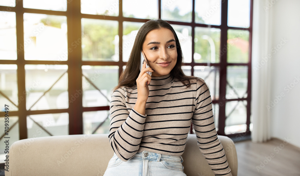Smiling millennial caucasian lady call by phone at sofa, talk in living room interior Smiling millennial caucasian lady call by phone at sofa, talk in living room interior