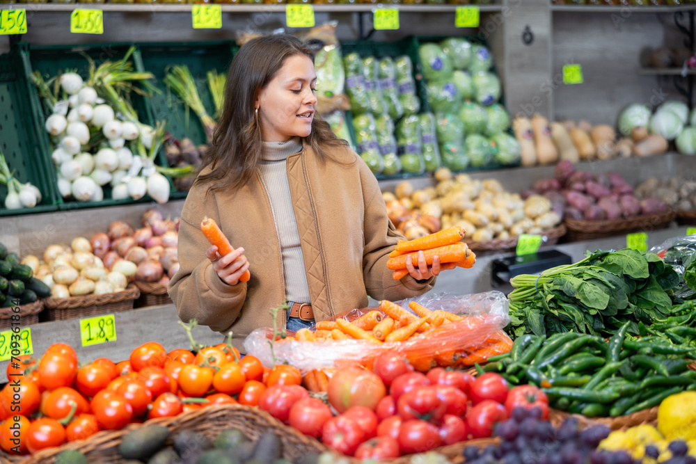 Girl purchaser choosing carrots at the counter in large grocery store