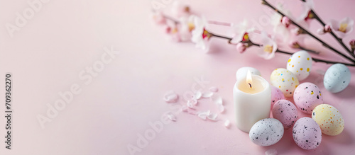 Burning white candle on pink table and background, pink blooming branch. Pastel eggs around candle. Calm, inspirational, minimalistic Easter card, banner. © Caphira Lescante