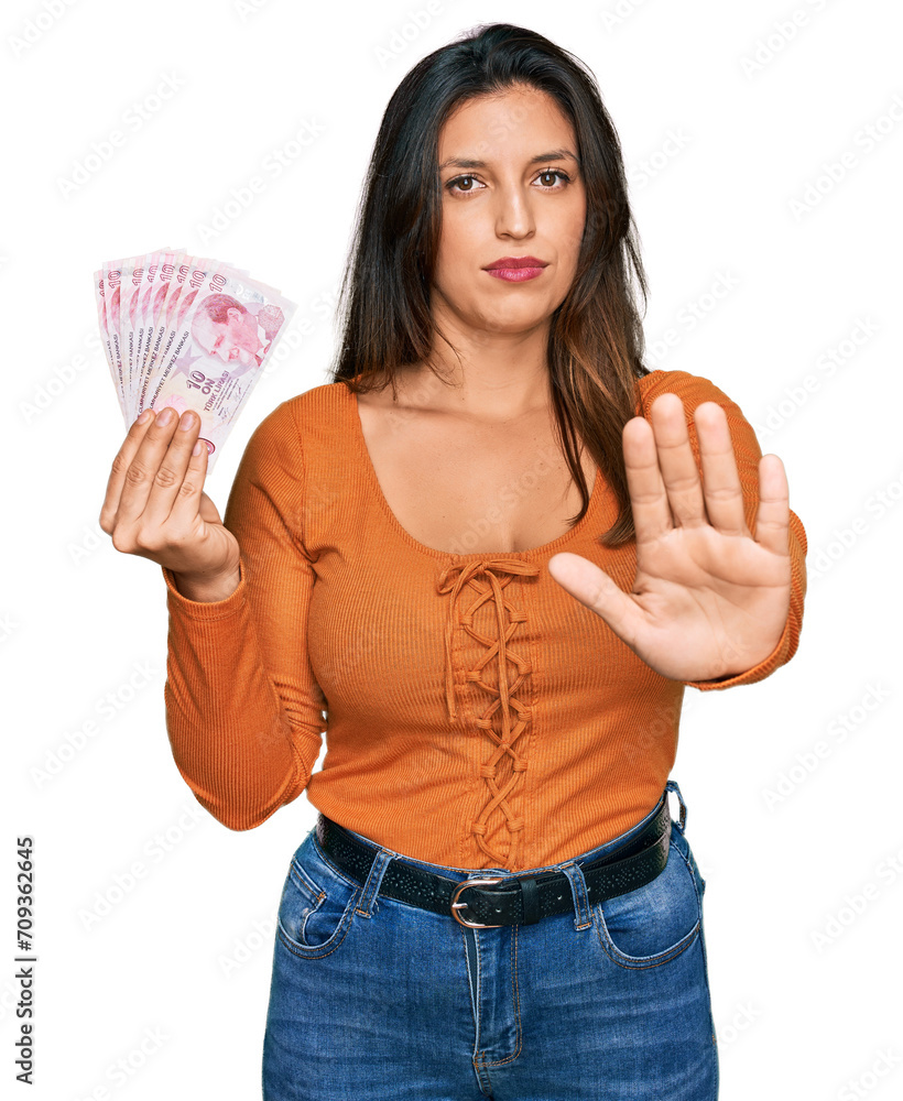 Beautiful hispanic woman holding 50 turkish lira banknotes with open hand doing stop sign with serious and confident expression, defense gesture Beautiful hispanic woman holding 50 turkish lira banknotes with open hand doing stop sign with serious and confident expression, defense gesture