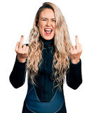 Young blonde woman wearing diver neoprene uniform showing middle finger doing fuck you bad expression, provocation and rude attitude. screaming excited