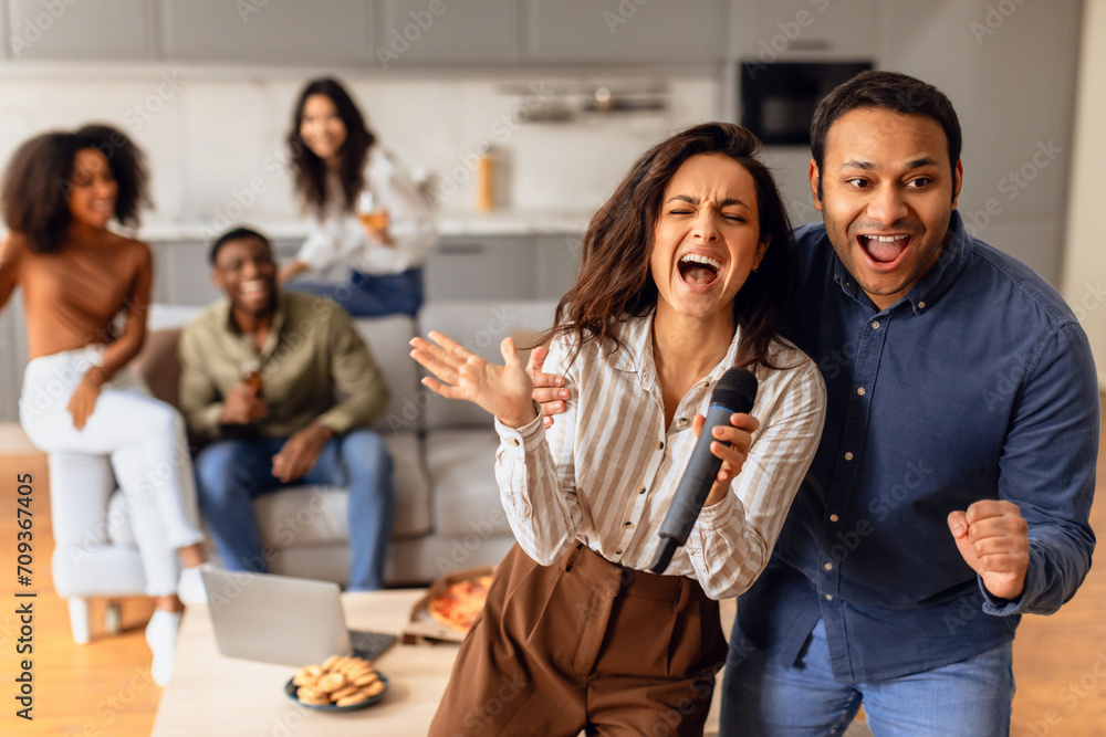 Obraz premium Diverse couple joyfully singing karaoke during students' party indoor