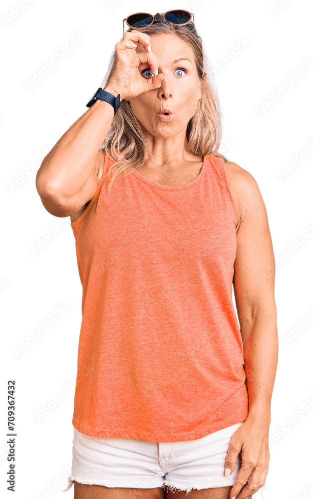 Middle age fit blonde woman wearing casual summer clothes and sunglasses doing ok gesture shocked with surprised face, eye looking through fingers. unbelieving expression. Middle age fit blonde woman wearing casual summer clothes and sunglasses doing ok gesture shocked with surprised face, eye looking through fingers. unbelieving expression.