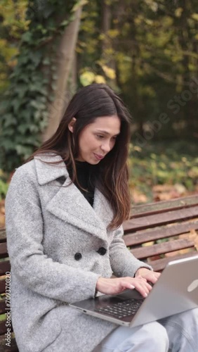 Young woman working in laptop outdoors and greeting coworker throguh device. She is happy and proud. photo