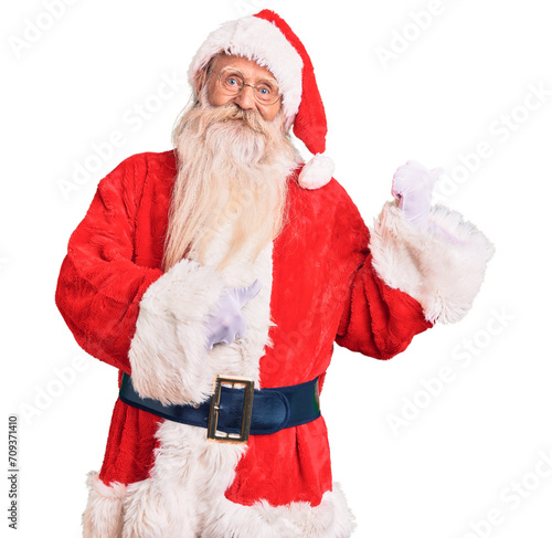 Old senior man with grey hair and long beard wearing traditional santa claus costume pointing to the back behind with hand and thumbs up, smiling confident