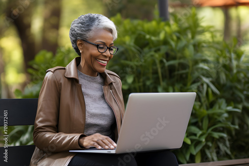 senior black woman working remotely on laptop in park - happiness digital nomad remote work business lifestyle concept