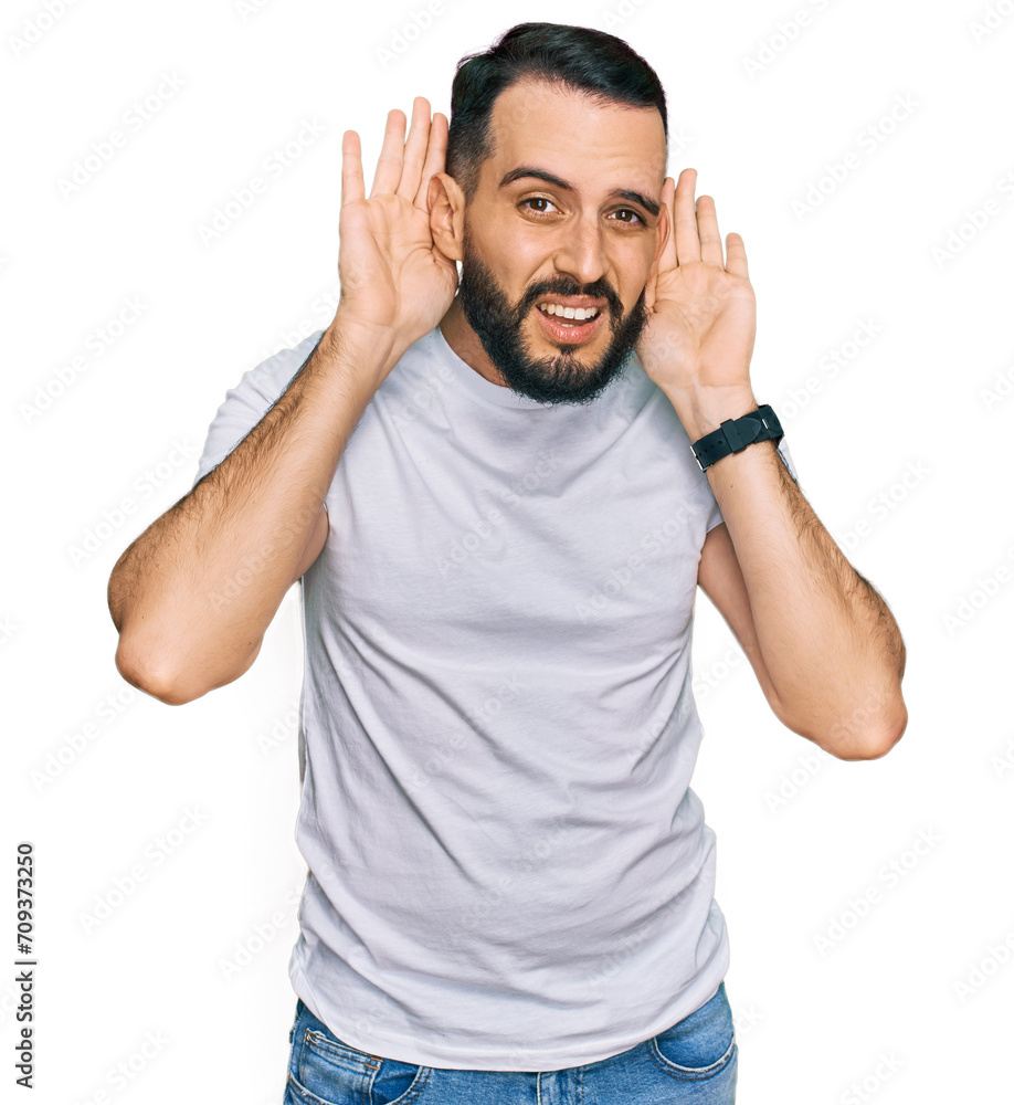 Young man with beard wearing casual white t shirt trying to hear both hands on ear gesture, curious for gossip. hearing problem, deaf Young man with beard wearing casual white t shirt trying to hear both hands on ear gesture, curious for gossip. hearing problem, deaf