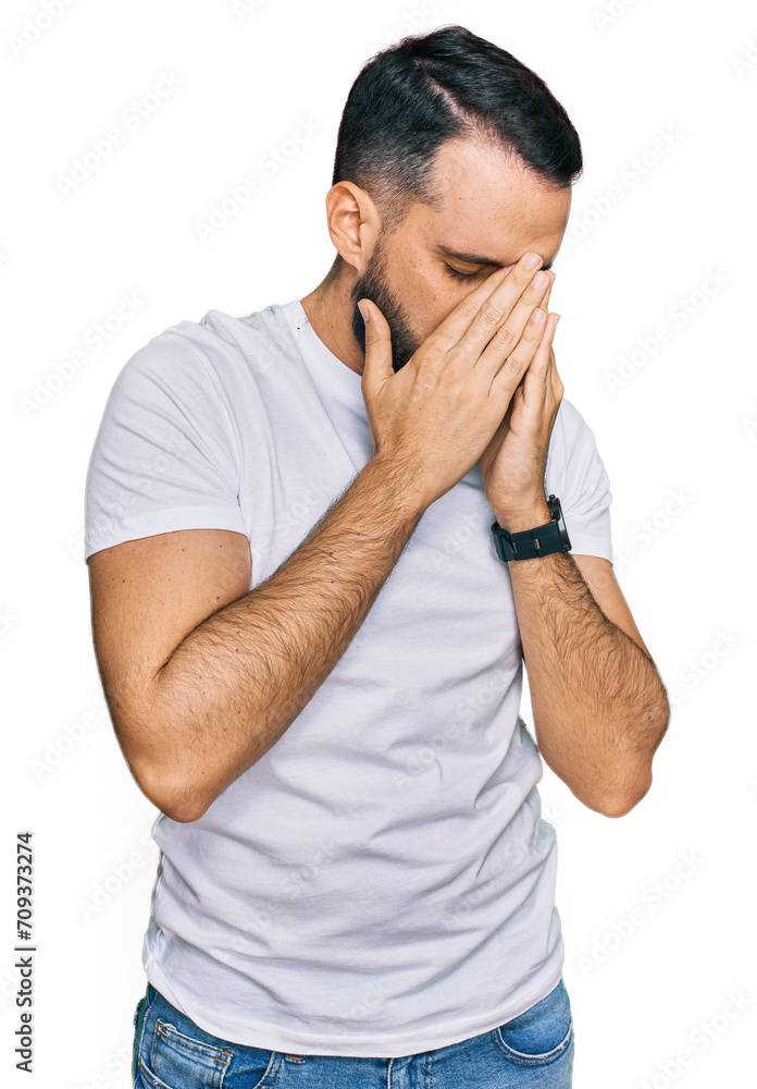 Young man with beard wearing casual white t shirt with sad expression covering face with hands while crying. depression concept. Young man with beard wearing casual white t shirt with sad expression covering face with hands while crying. depression concept.