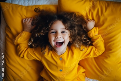 Cute little girl with curly hair lying in bed and yawning