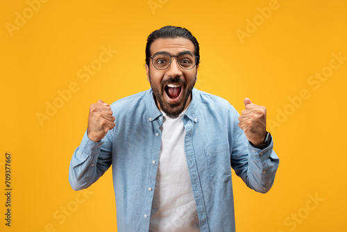 Euphoric man in blue denim shirt with clenched fists and mouth wide open