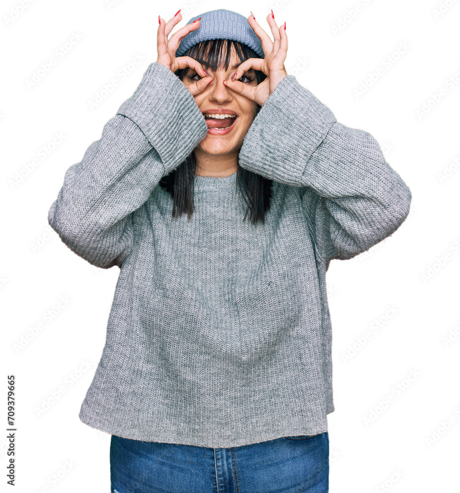 Young hispanic woman wearing cute wool cap doing ok gesture like binoculars sticking tongue out, eyes looking through fingers. crazy expression. Young hispanic woman wearing cute wool cap doing ok gesture like binoculars sticking tongue out, eyes looking through fingers. crazy expression.