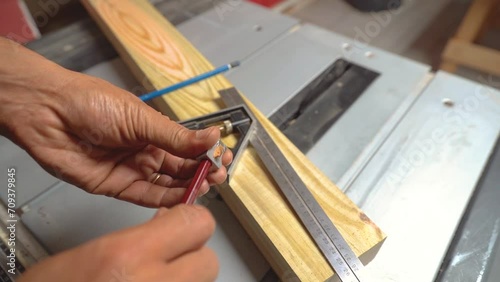 A woodworker is sharpening his pencils before he starts measuring and marking a board of pine. On the frame we can also see a table saw with a board of treated pine and a composition square on top. photo