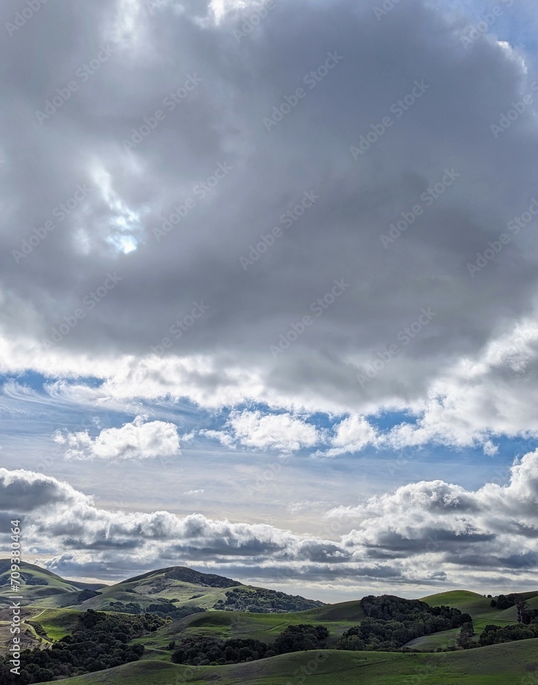 rolling hills embraced by turbulent clouds, forming a celestial window in the sky