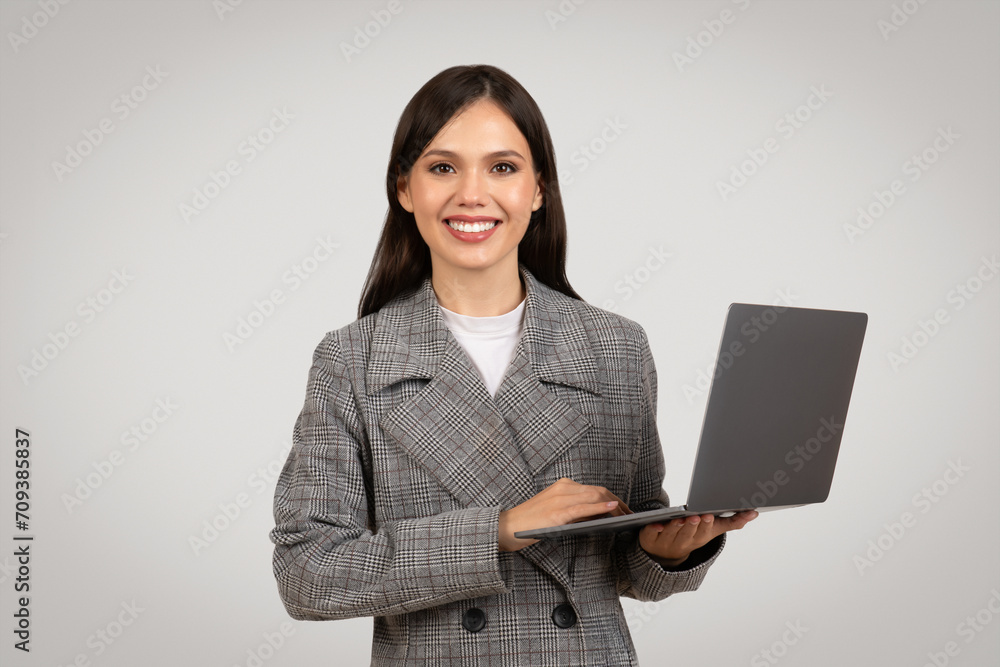 Smiling businesswoman presenting laptop in checkered suit, tech savvy Smiling businesswoman presenting laptop in checkered suit, tech savvy