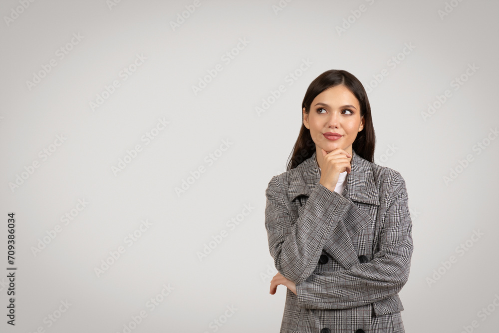Thoughtful woman in blazer touching chin and looking aside at free space Thoughtful woman in blazer touching chin and looking aside at free space