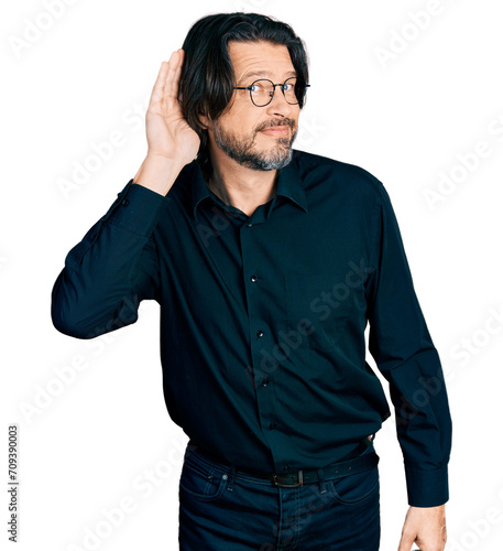 Middle age caucasian man wearing casual clothes and glasses smiling with hand over ear listening an hearing to rumor or gossip. deafness concept.