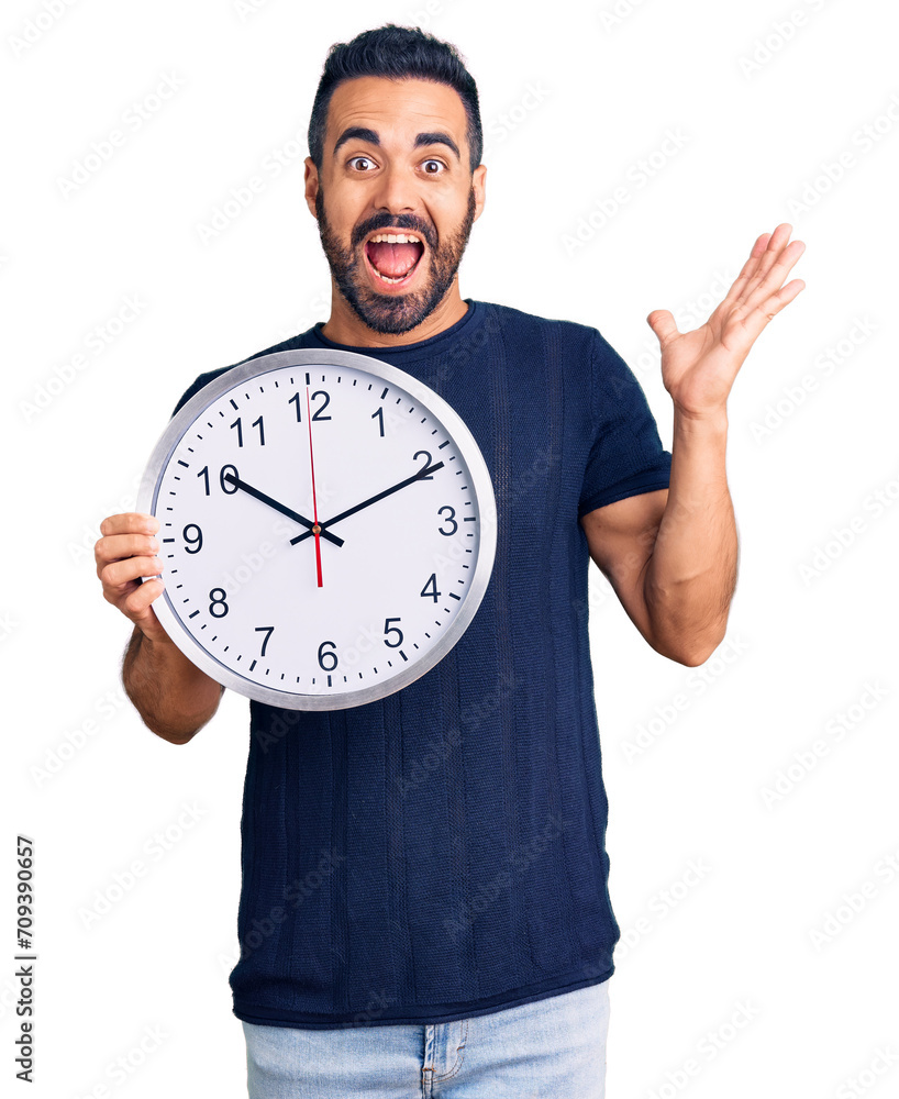 Young hispanic man holding big clock celebrating victory with happy smile and winner expression with raised hands Young hispanic man holding big clock celebrating victory with happy smile and winner expression with raised hands