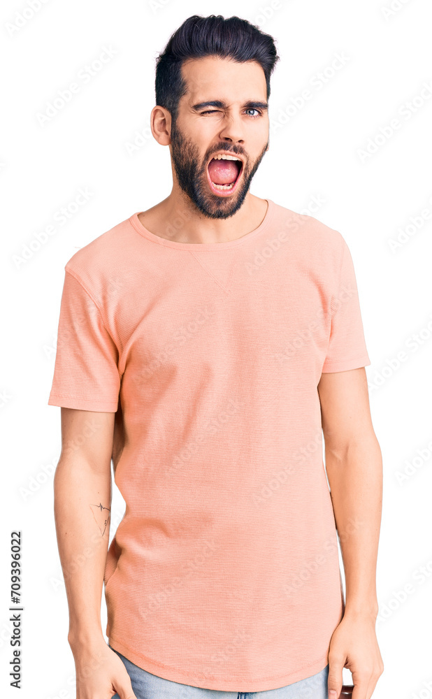 Young handsome man with beard wearing casual t-shirt winking looking at the camera with sexy expression, cheerful and happy face. Young handsome man with beard wearing casual t-shirt winking looking at the camera with sexy expression, cheerful and happy face.