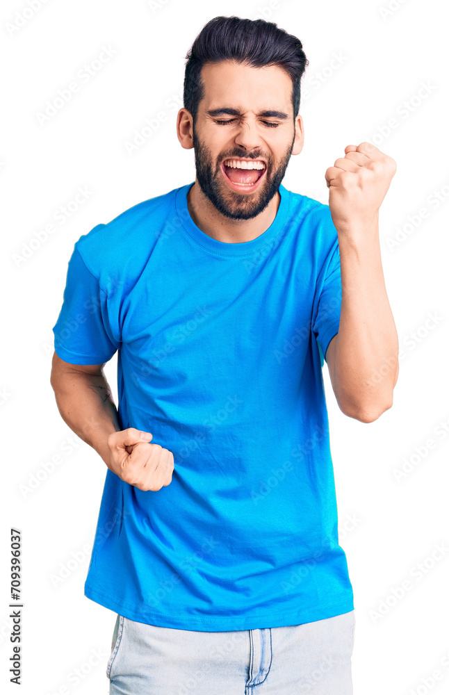 Young handsome man with beard wearing casual t-shirt celebrating surprised and amazed for success with arms raised and eyes closed. winner concept. Young handsome man with beard wearing casual t-shirt celebrating surprised and amazed for success with arms raised and eyes closed. winner concept.