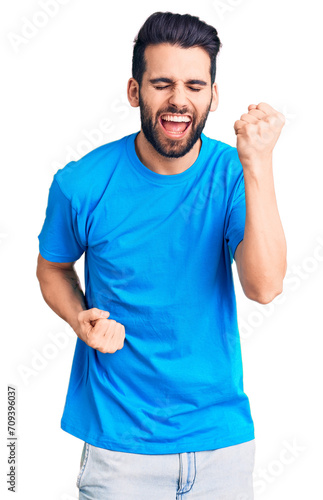 Young handsome man with beard wearing casual t-shirt celebrating surprised and amazed for success with arms raised and eyes closed. winner concept.