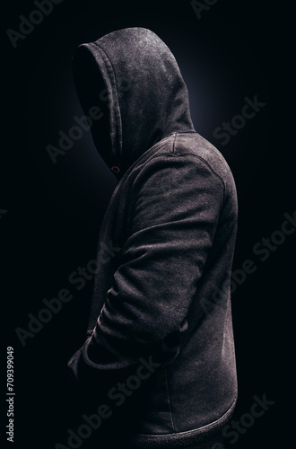 Photo of scary shaded hooded man standing and looking on dark background.