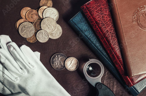 Photo of numismatist table upper view with white gloves, coins and album book holders. photo