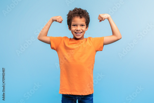 Strong, confident boy flexing muscles on blue background