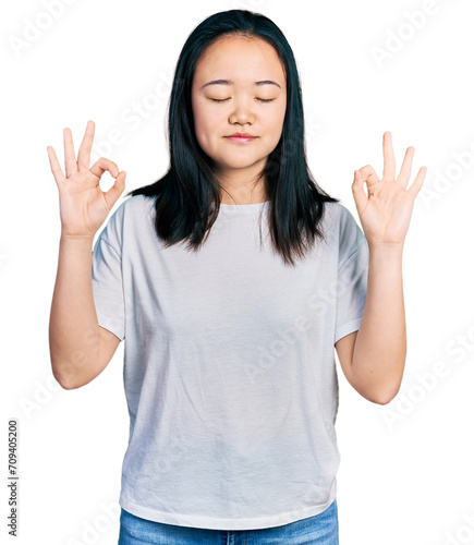 Young chinese woman wearing casual white t shirt relax and smiling with eyes closed doing meditation gesture with fingers. yoga concept.