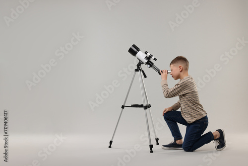 Little boy looking at stars through telescope on light grey background, space for text
