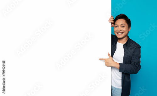 Happy Asian man in casual attire peeking around a large blank white banner