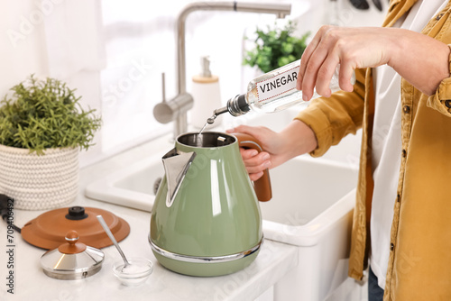 Woman pouring vinegar from bottle into electric kettle in kitchen, closeup photo