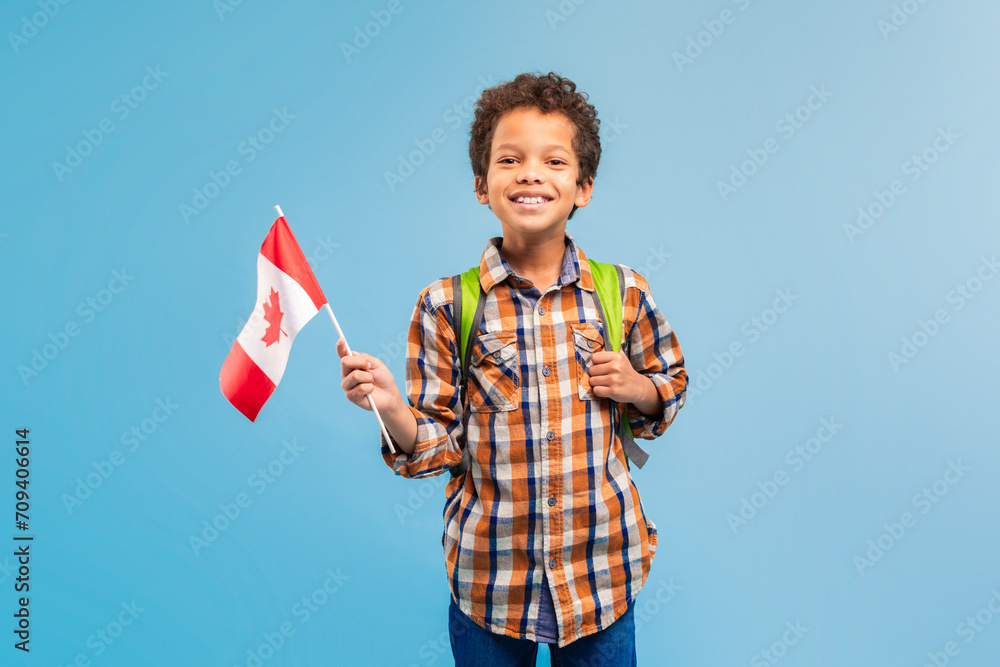 Happy boy with Canadian flag and backpack, blue backdrop Happy boy with Canadian flag and backpack, blue backdrop