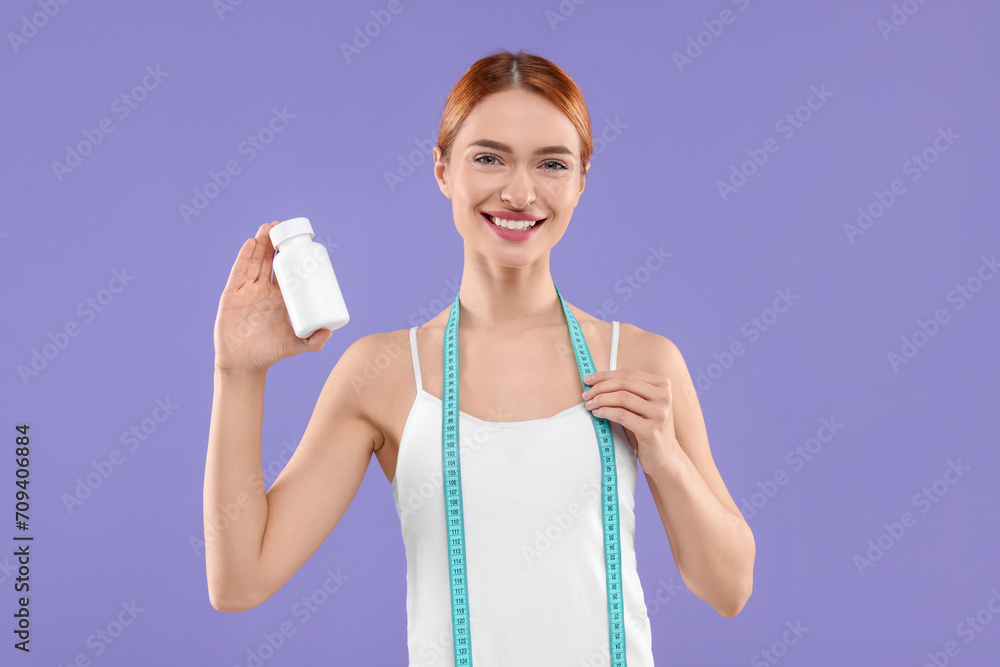 Happy young woman with bottle of pills and measuring tape on purple background. Weight loss Happy young woman with bottle of pills and measuring tape on purple background. Weight loss