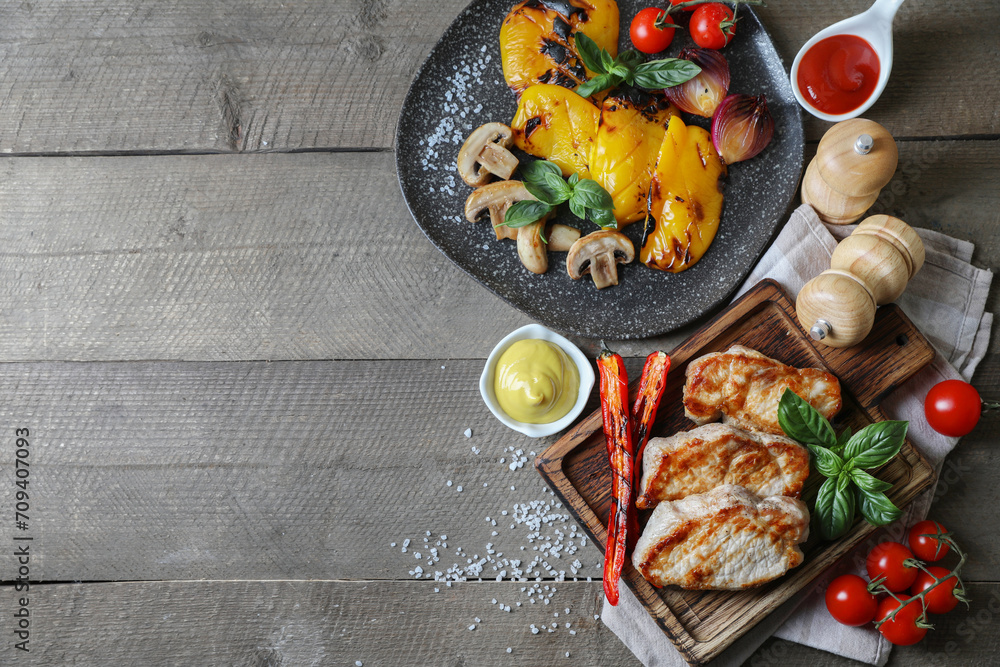 Delicious grilled meat and vegetables served with sauces on wooden table, flat lay. Space for text