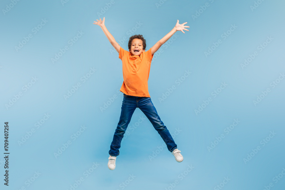 Joyful boy jumping with arms wide open on blue background