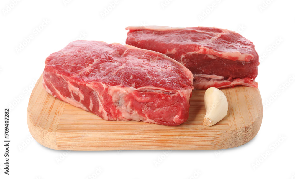 Board with steaks of raw beef meat and garlic clove isolated on white