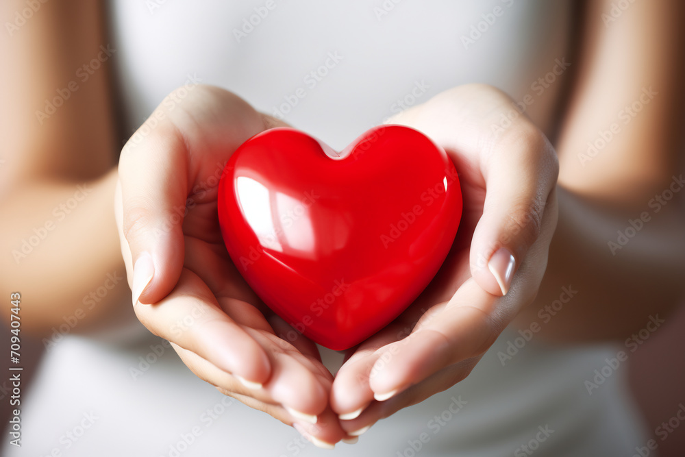 Obraz premium Close-up of Woman's Hands Gently Holding a Glossy Red Heart, Love and Care Concept