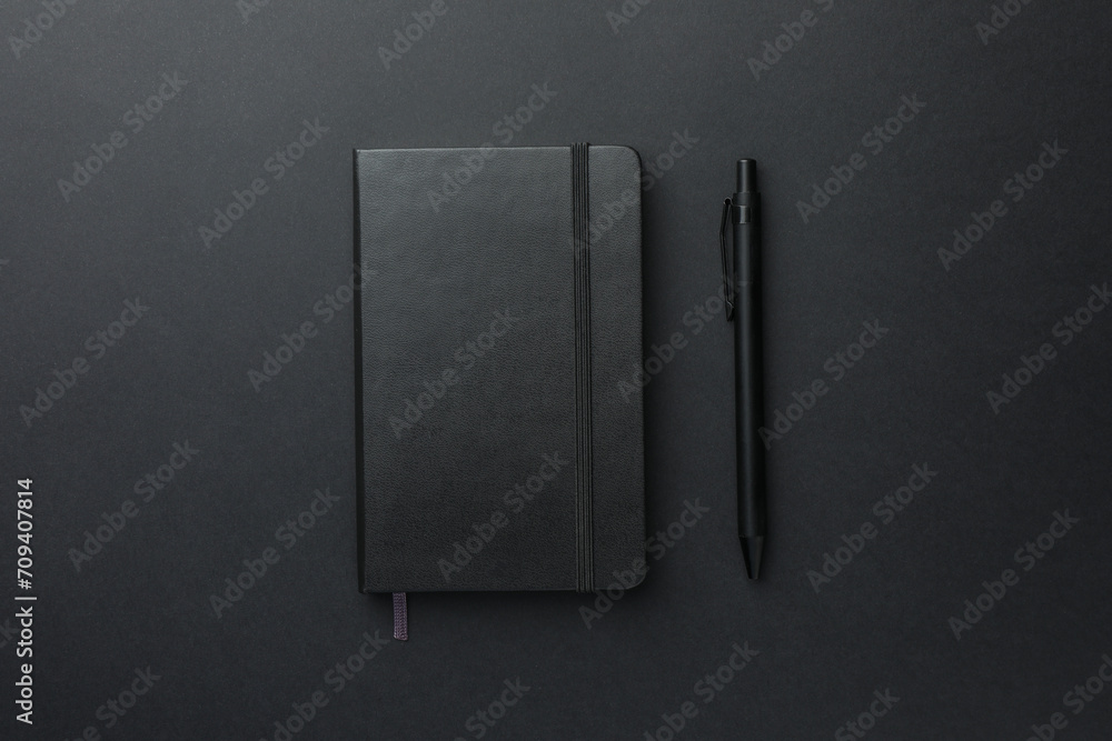 Closed notebook and pen on black background, top view Closed notebook and pen on black background, top view