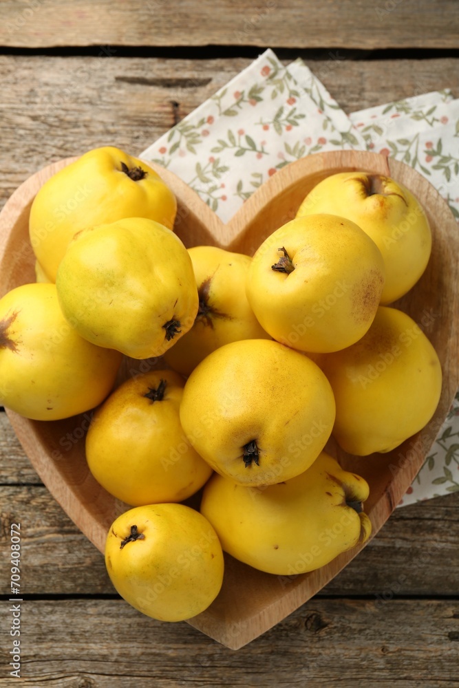 Tasty ripe quinces in heart shaped bowl on wooden table, top view