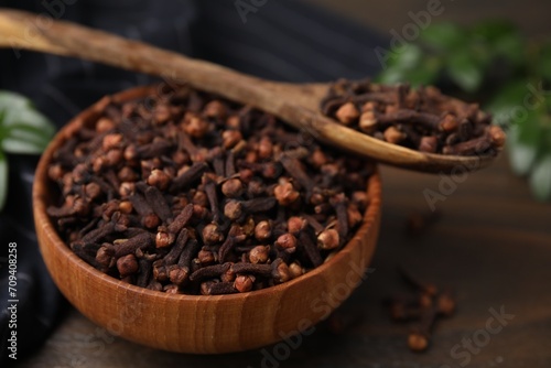 Bowl and spoon with aromatic cloves on wooden table, closeup