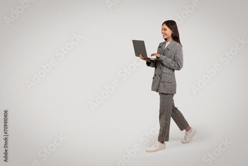 Businesswoman walking with laptop, smiling, copy space © Prostock-studio