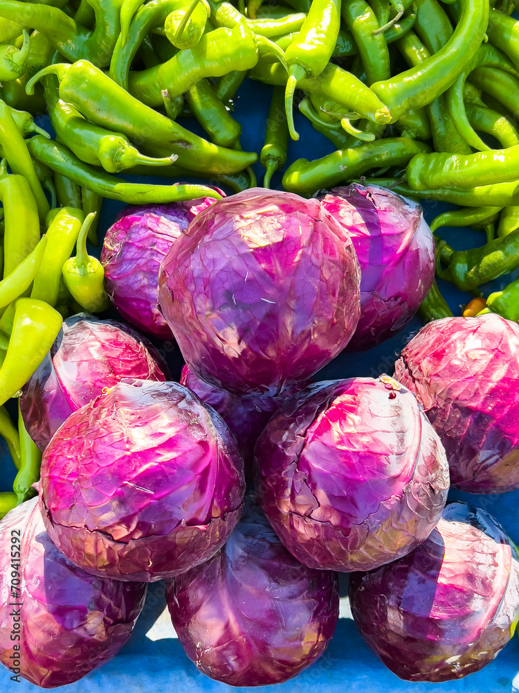 Sun shines on a pile of red cabbage stacked in front of green chilli peppers at a farmers' market, side view. Beautiful food background with copy space, close up. Farm full of organic vegetables. Sun shines on a pile of red cabbage stacked in front of green chilli peppers at a farmers' market, side view. Beautiful food background with copy space, close up. Farm full of organic vegetables.